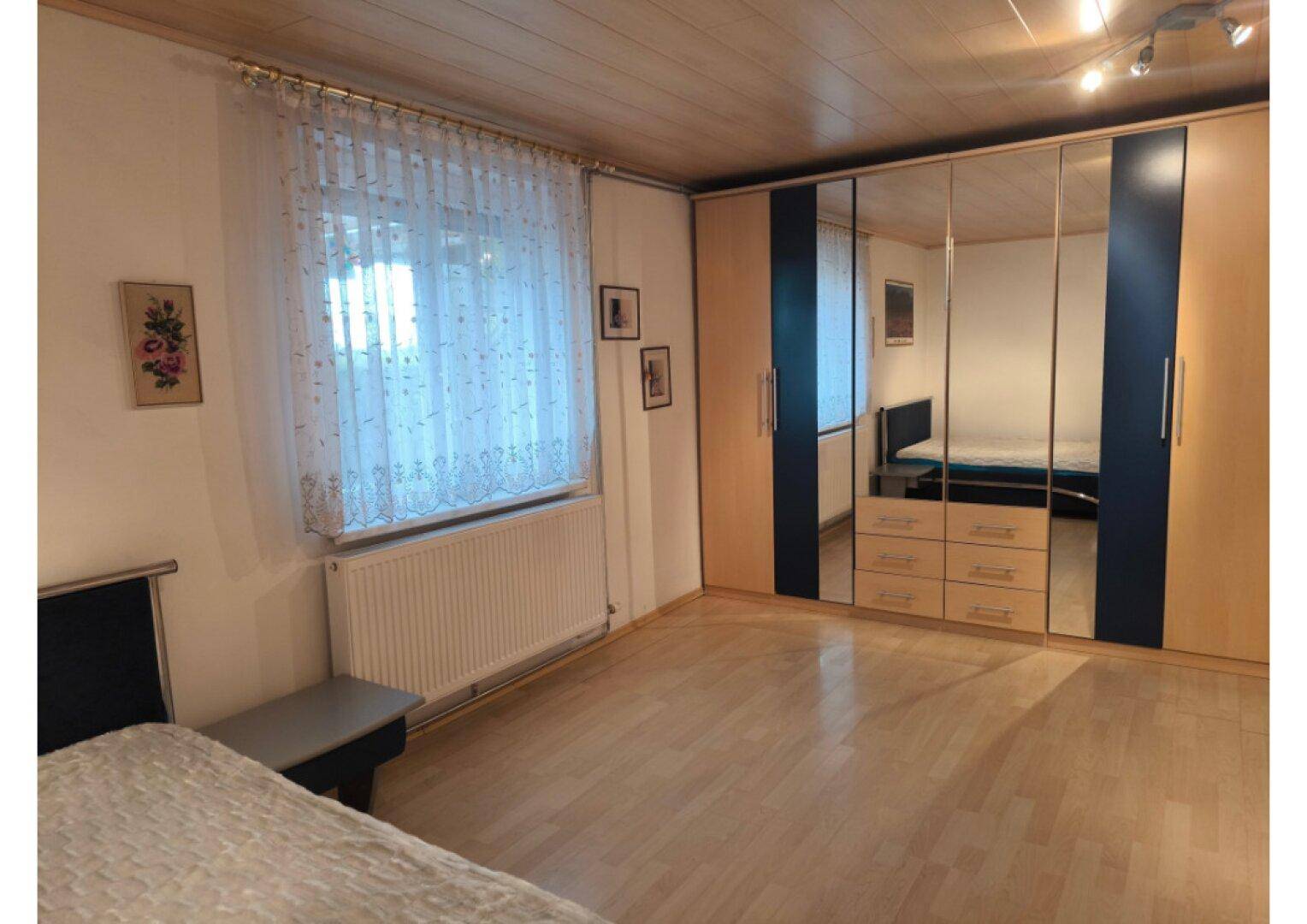 Geräumiges Schlafzimmer mit hellem Holzfußboden und einem großen Spiegelschrank.
