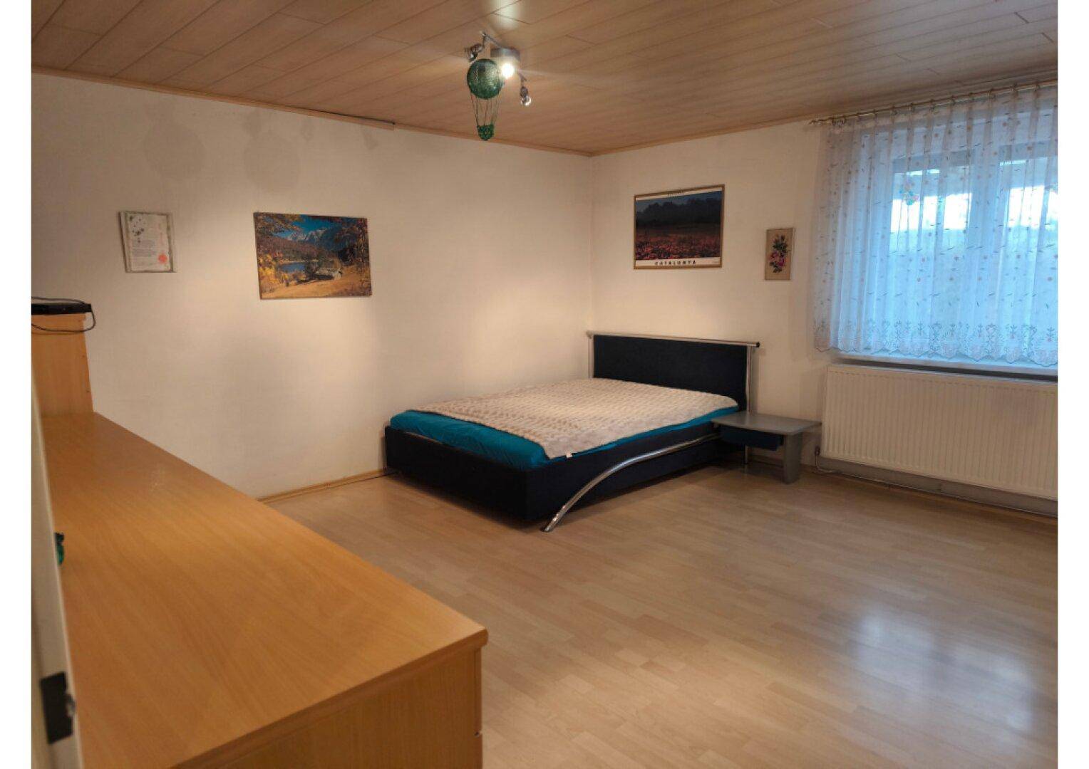 Schlafzimmer mit Holzboden, einem modernen Bett und einem Fenster mit Vorhängen.