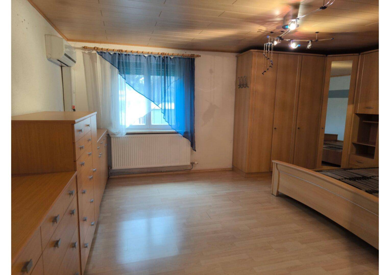 Schlafzimmer mit Holzboden, großem Kleiderschrank, Kommode und Klimaanlage.