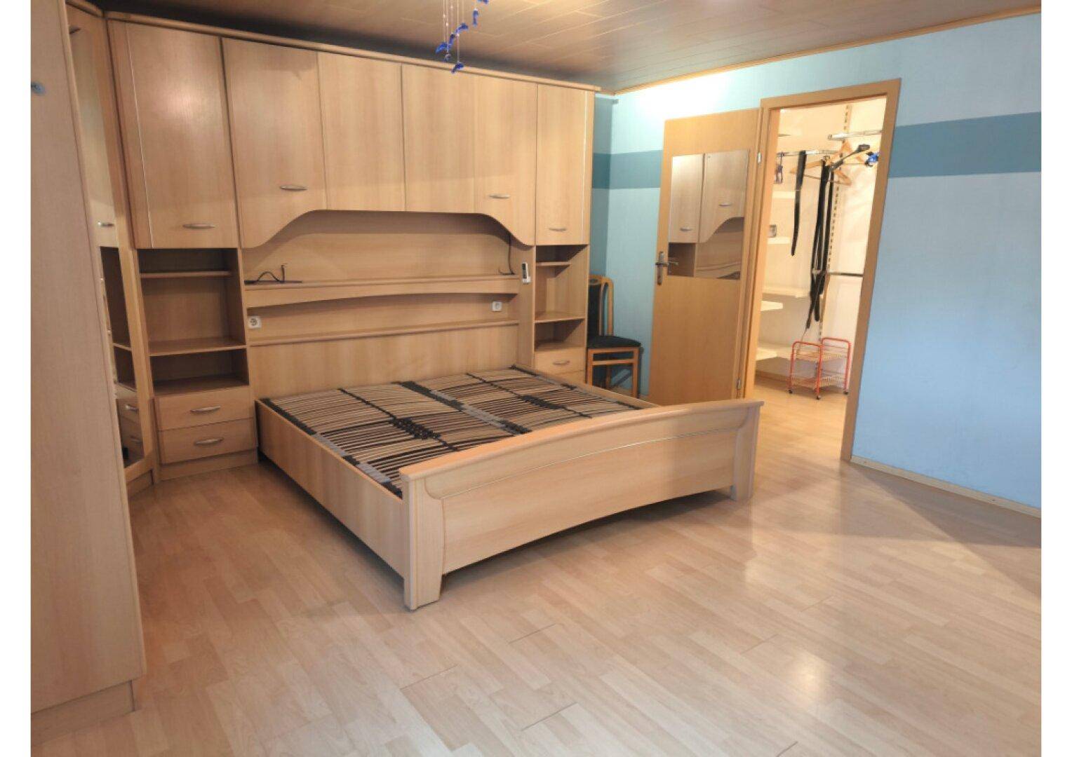 Helles Schlafzimmer mit Holzfußboden, integriertem Bett und Zugang zu einem begehbaren Kleiderschrank.