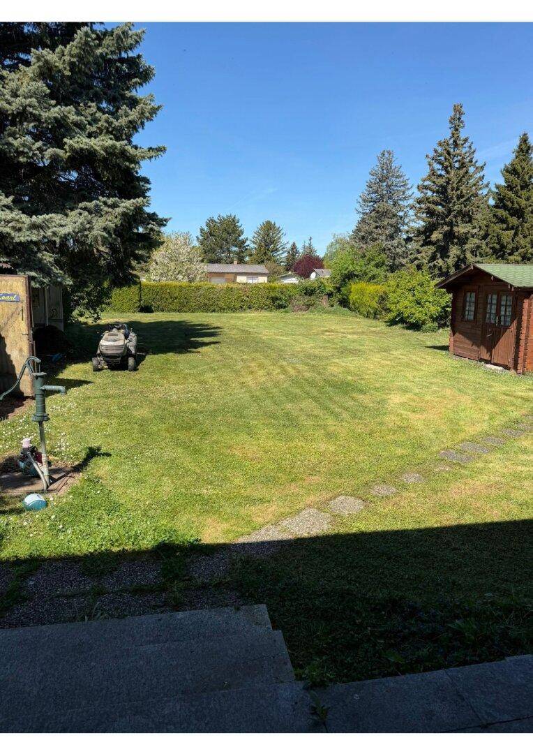 Weitläufiger Garten mit Rasenfläche, Bäumen, einem Gartenhaus und einer Wasserpumpe.