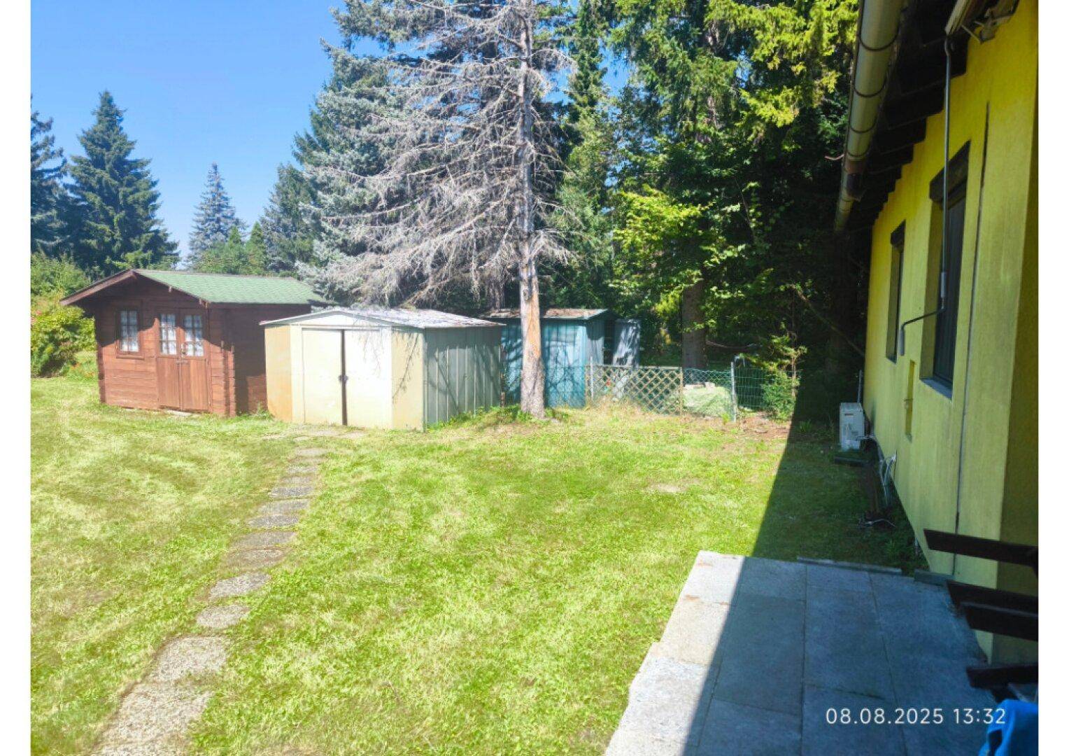 Weitläufiger Garten mit Rasen, hohen Bäumen und mehreren Gartenhäusern im Hintergrund.