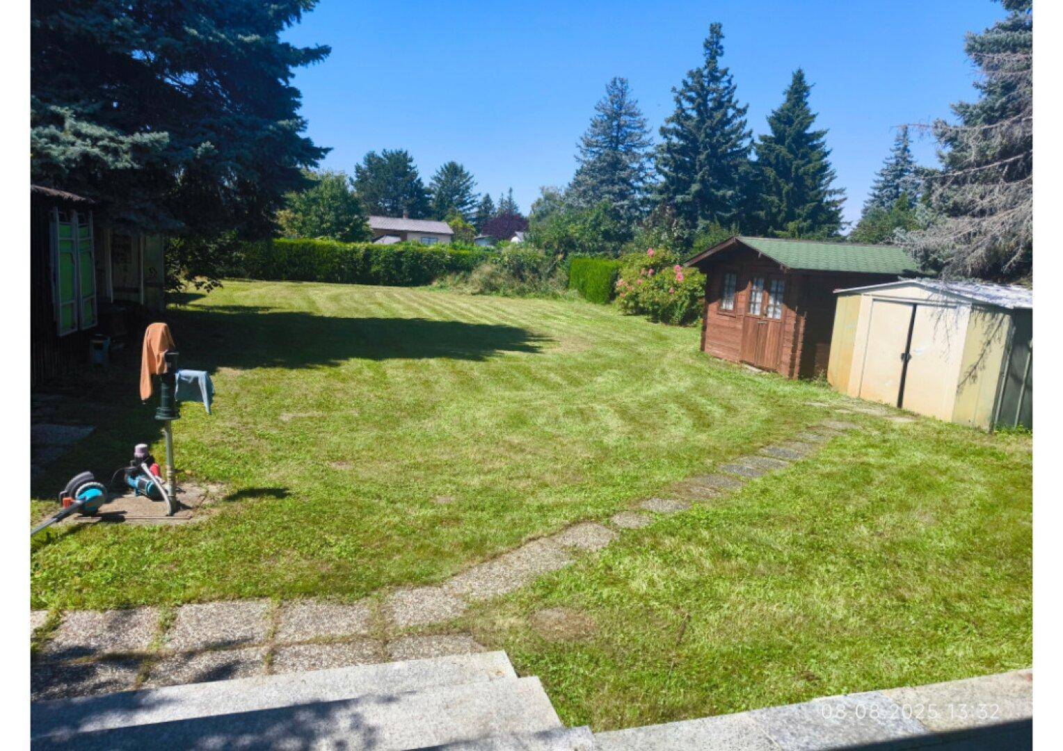 Großer Garten mit Rasenfläche, Gartenhäusern und einem gepflasterten Weg.