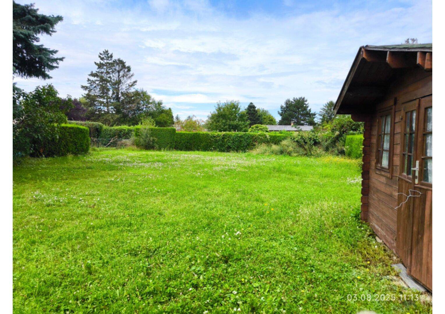 Weitläufiger, grüner Garten mit Rasenfläche und Hecken unter bewölktem Himmel.