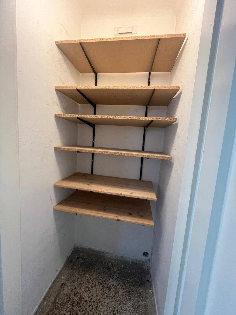 Kleiner Abstellraum mit einfachen Holzregalen und unfertigem Boden.