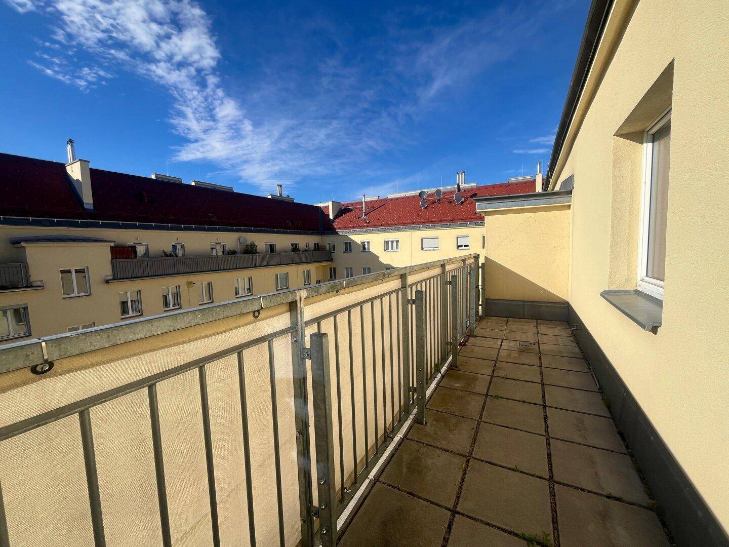 Langer Balkon mit Fliesenboden und Blick auf den ruhigen Innenhof des Gebäudes.