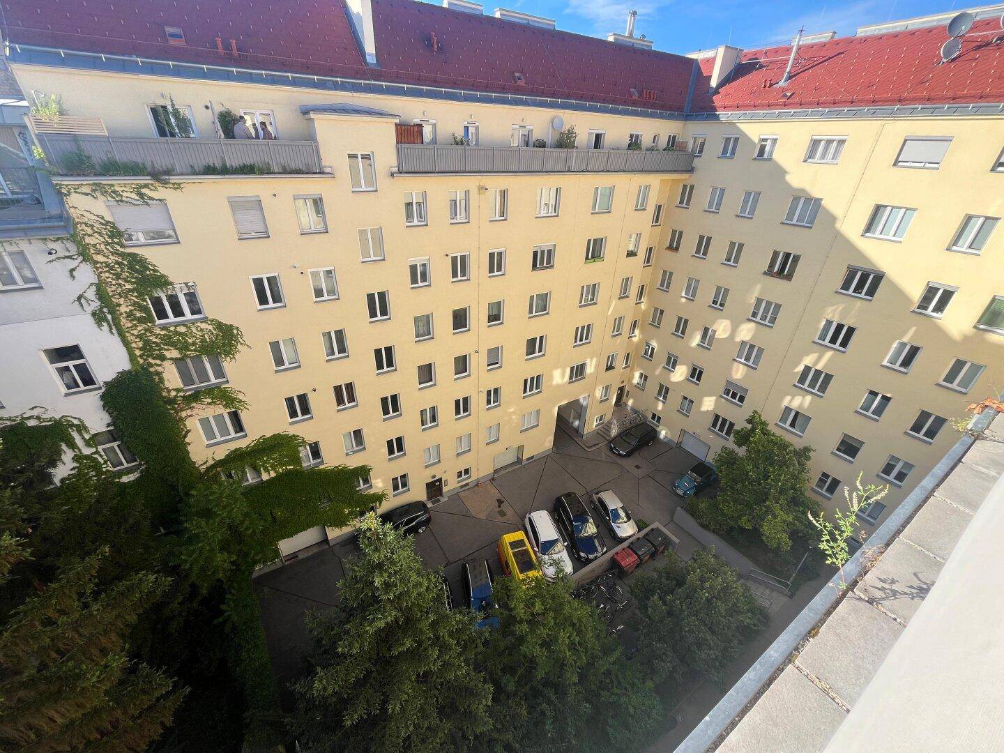 Blick von oben auf einen begrünten Innenhof mit parkenden Autos und umliegenden Wohngebäuden.