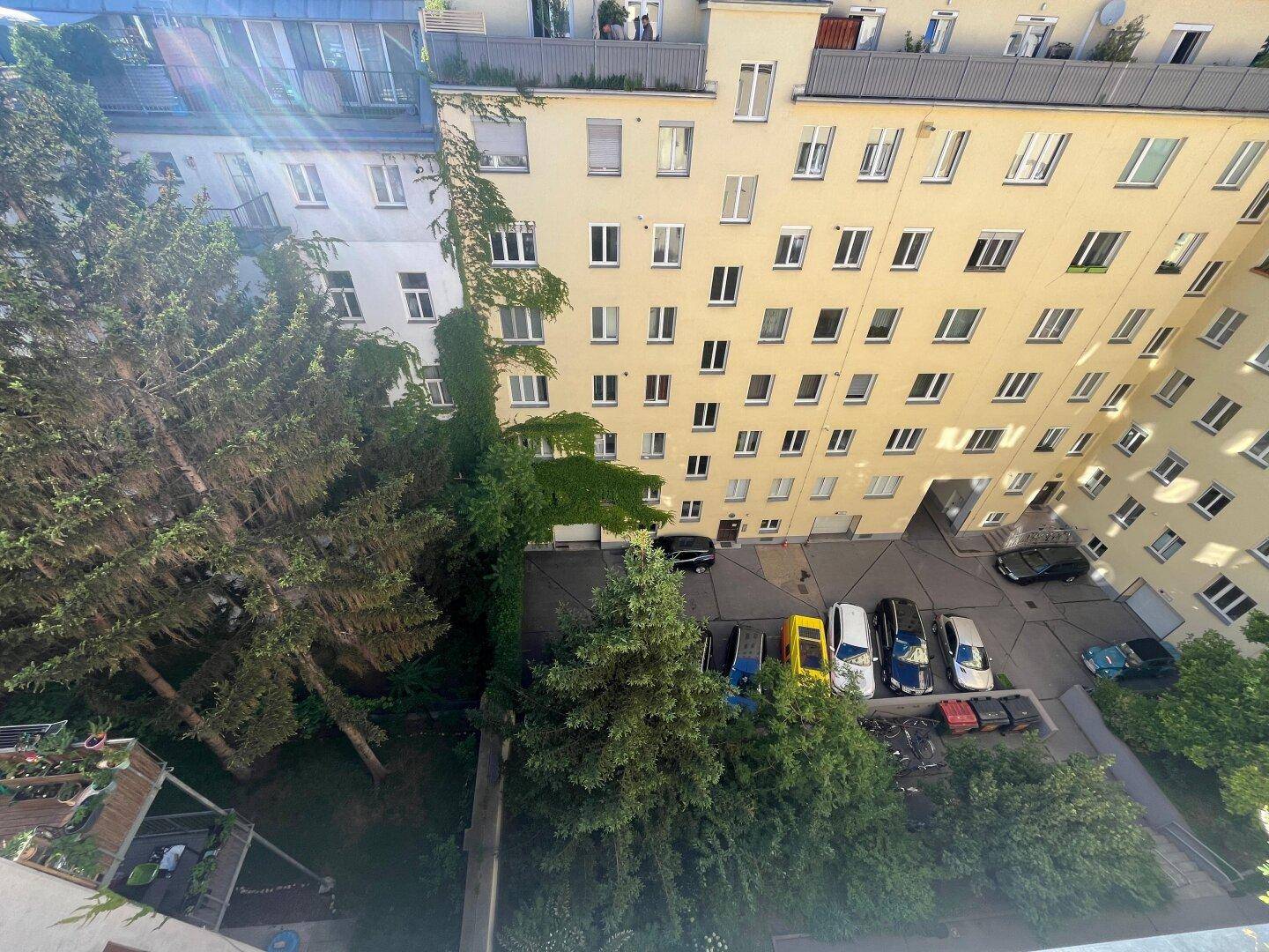 Weitläufiger Innenhof mit Bäumen und Parkplätzen, umgeben von hohen Wohngebäuden.