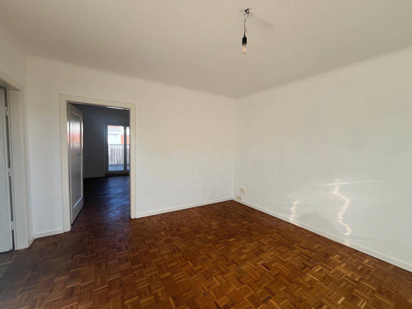 Leeres Zimmer mit klassischem Parkettboden und offenem Durchgang zu einem weiteren Raum.