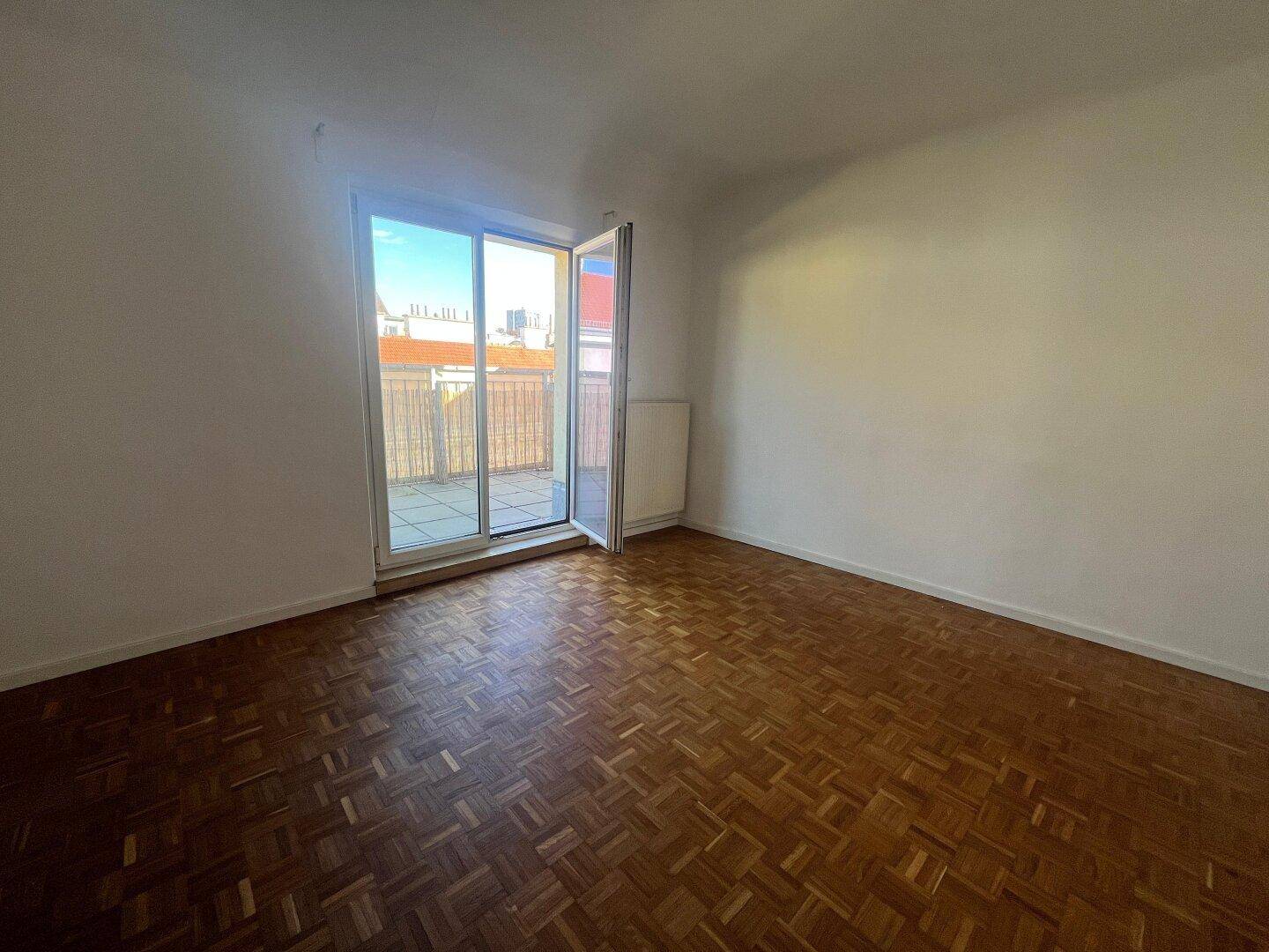 Geräumiges Zimmer mit Parkettboden und großen Fenstertüren, die auf einen Balkon führen.