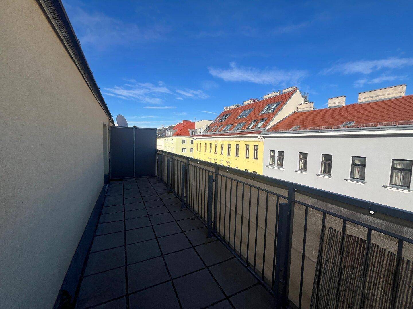 Langer, gefliester Balkon mit Metallgeländer und Blick auf die umliegenden Dächer.