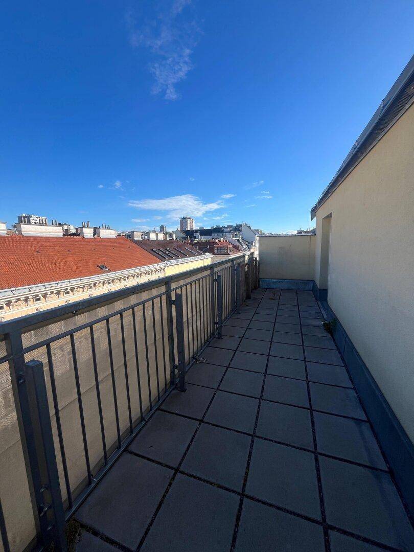 Sonniger Balkon mit Fliesenboden und Blick auf die Dächer der Nachbargebäude.