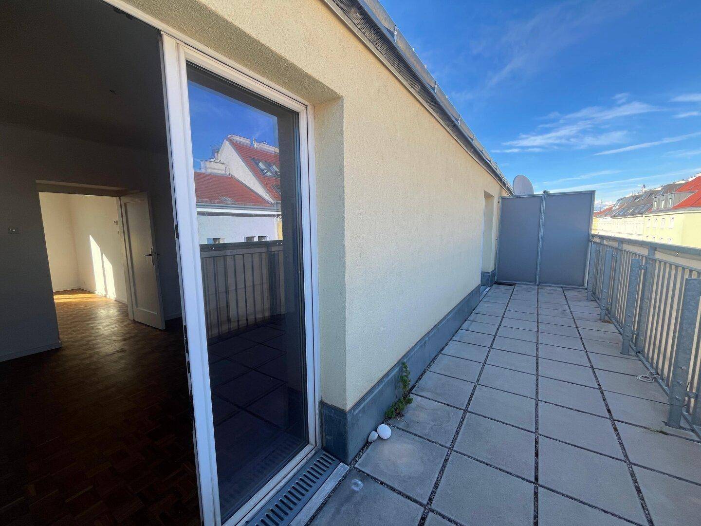 Balkon mit Fliesenboden und Zugang durch eine große Glastür zu einem Innenraum.
