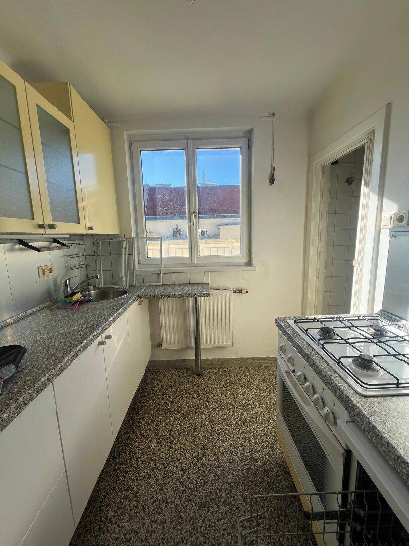 Funktionale Küche mit hellen Schränken, Granit-Arbeitsplatte und Gasherd unter einem Fenster.