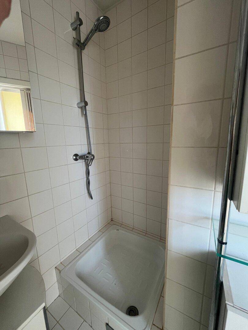 Kleines Badezimmer mit weiß gefliestem Duschbereich und einfacher Duscharmatur.