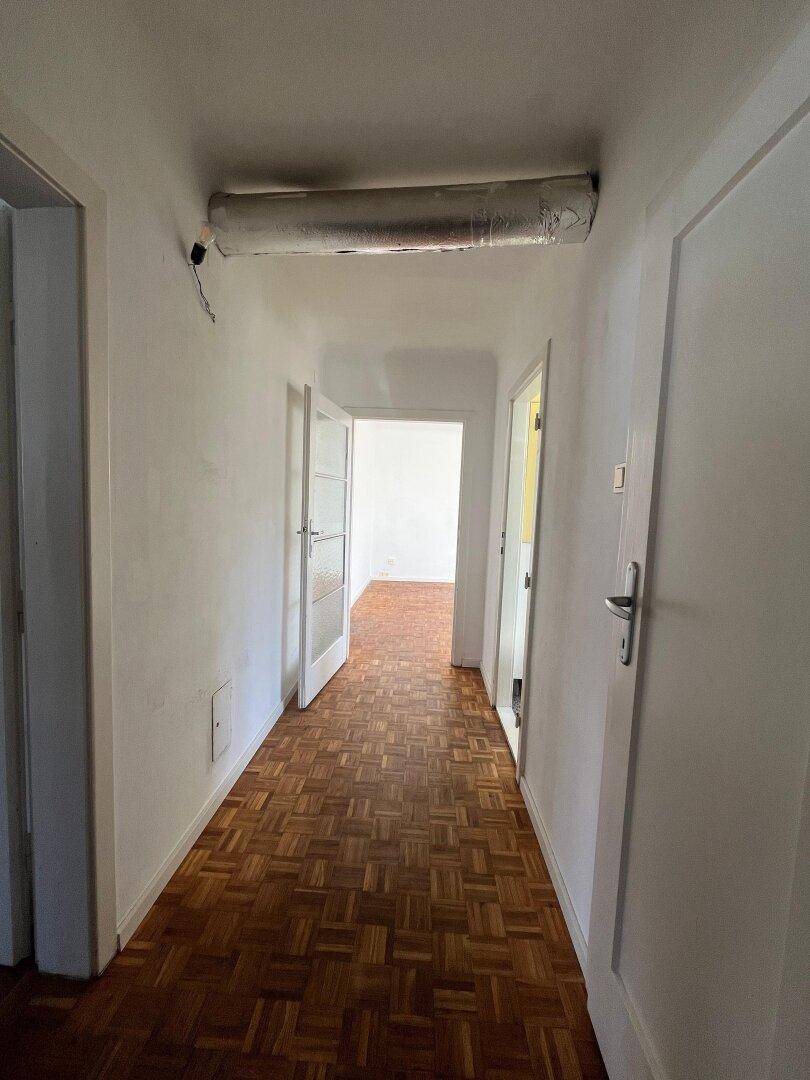 Langer Flur mit Fischgrätparkettboden und weißen Türen, der zu weiteren Räumen führt.