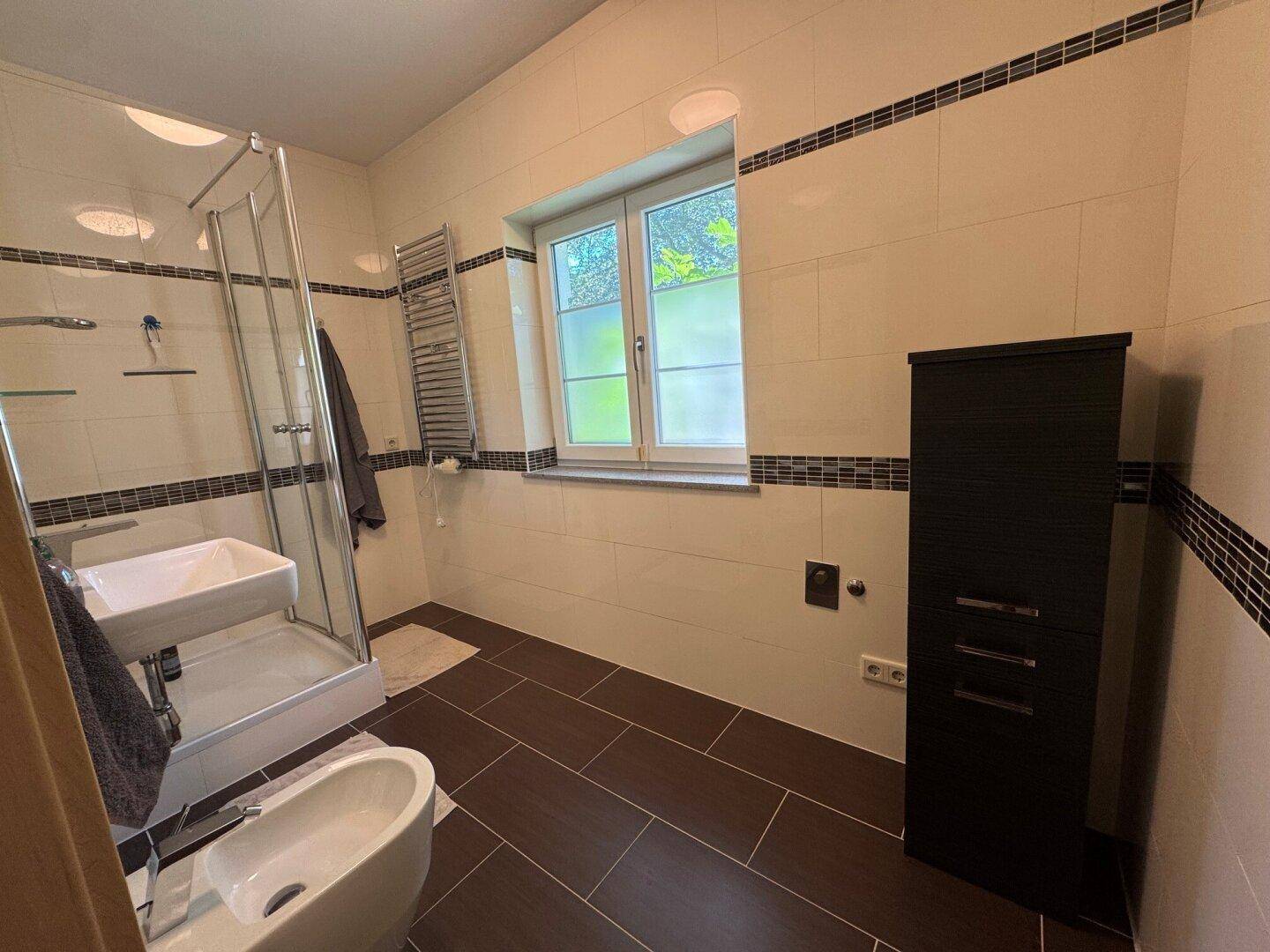 Modernes Badezimmer mit Dusche, Bidet, Fenster und dunklen Bodenfliesen.