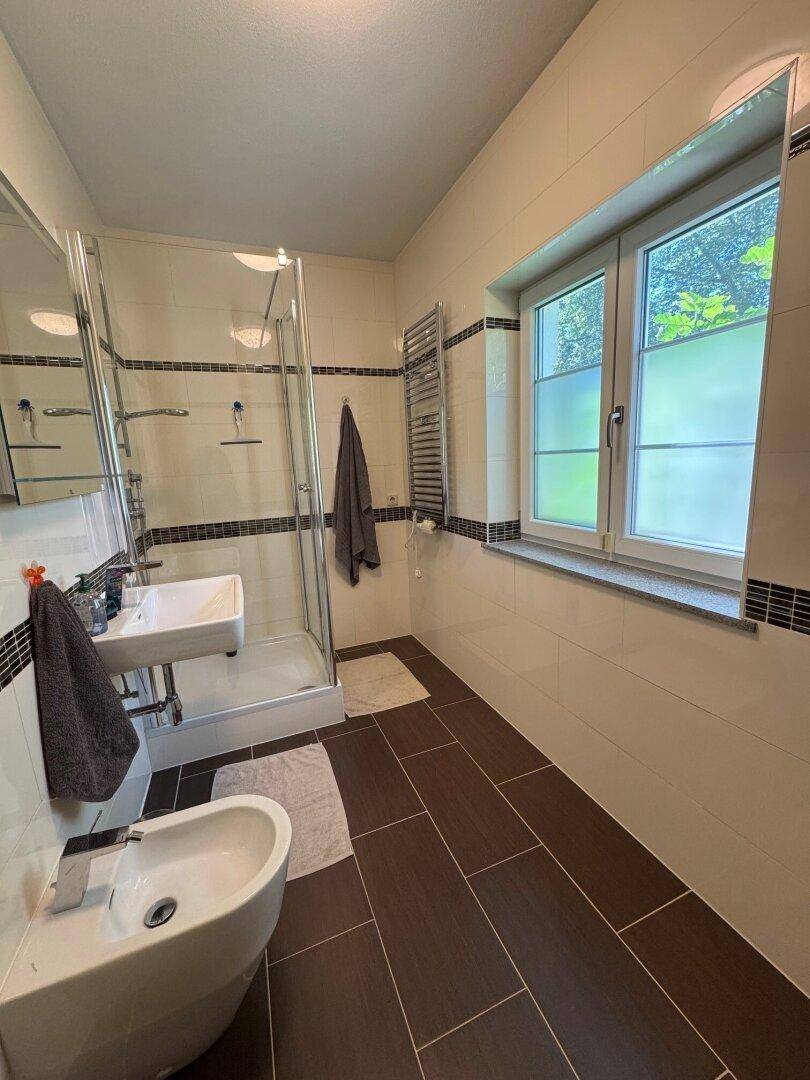 Helles Badezimmer mit Duschkabine, Bidet und Fenster für Tageslicht.