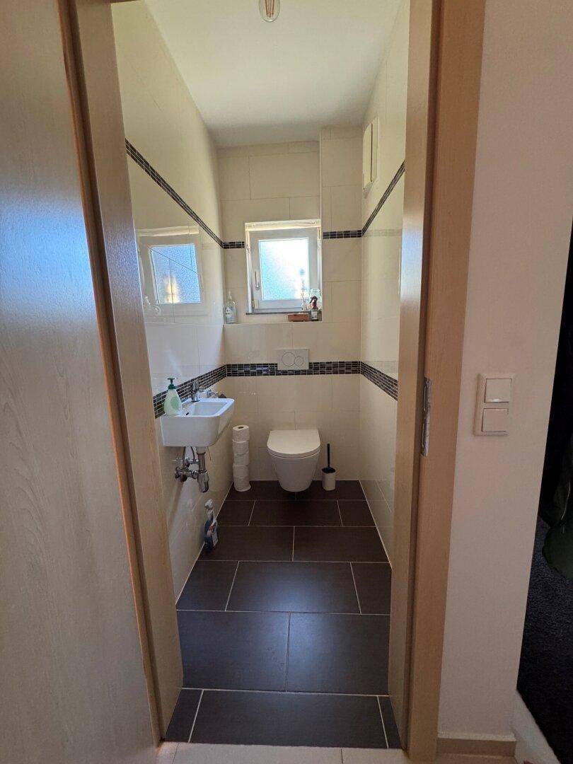 Kleines Gäste-WC mit Fenster, Waschbecken und dunklen Bodenfliesen.