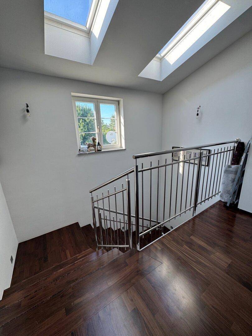 Treppenhaus mit Holzstufen, Metallgeländer und Oberlichtern für viel Tageslicht.