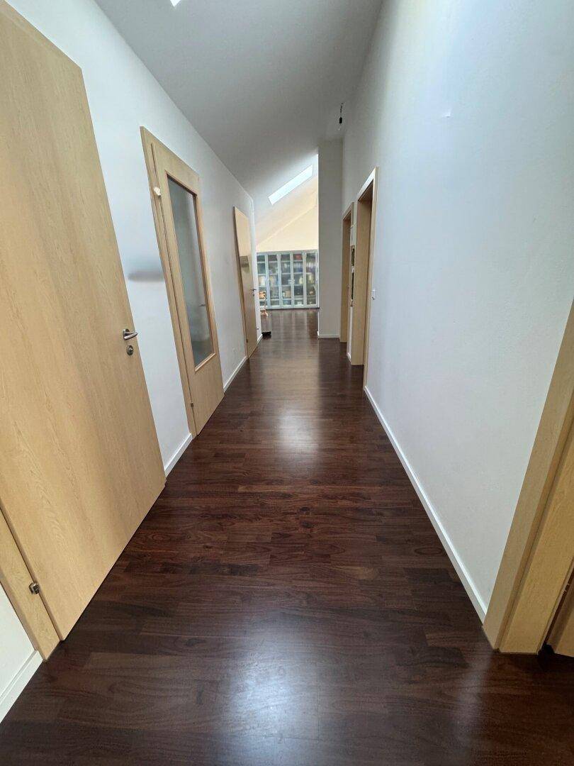 Langer Flur mit dunklem Holzfußboden und schrägen Decken im Dachgeschoss.