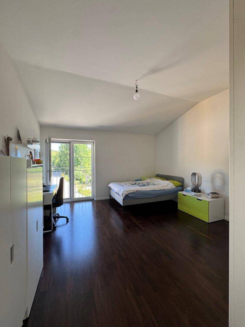 Geräumiges Schlafzimmer mit dunklem Holzfußboden und Zugang zu einem französischen Balkon.