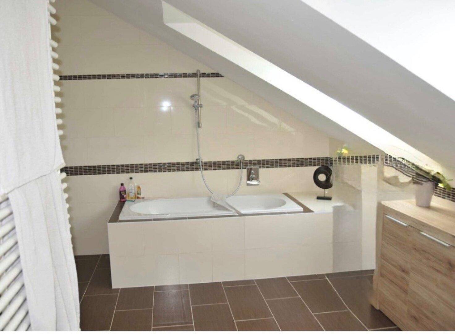 Badezimmer im Dachgeschoss mit Badewanne, Dachschräge und Fliesenboden.