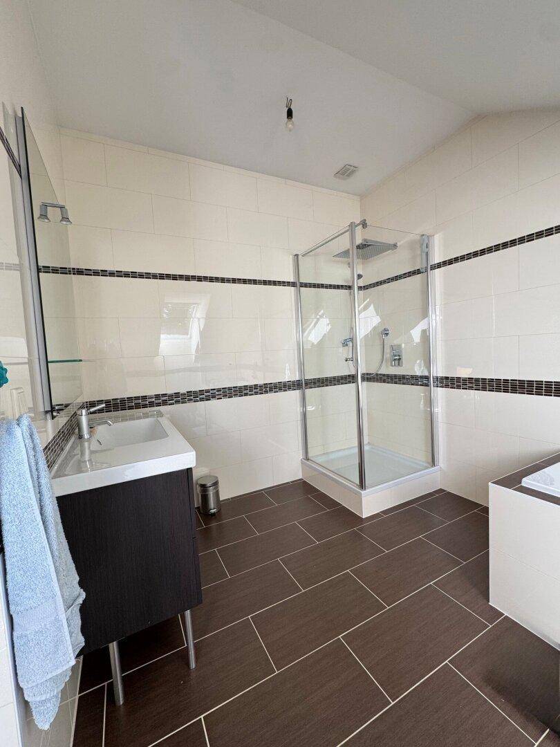 Modernes Badezimmer im Dachgeschoss mit Dusche, Waschbecken und Fliesenboden.