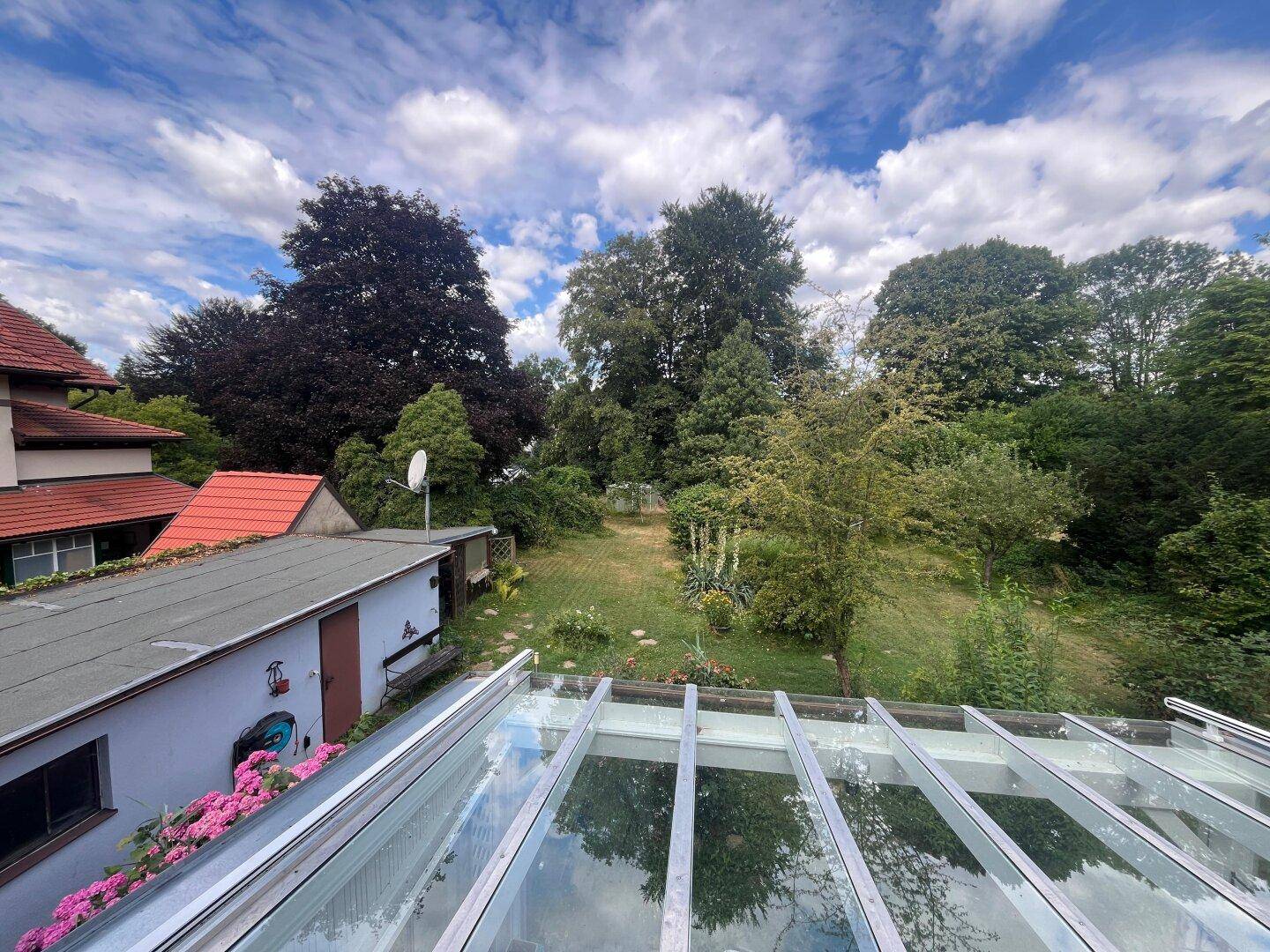 Weitläufiger Gartenbereich mit altem Baumbestand und Blick auf ein Nebengebäude.