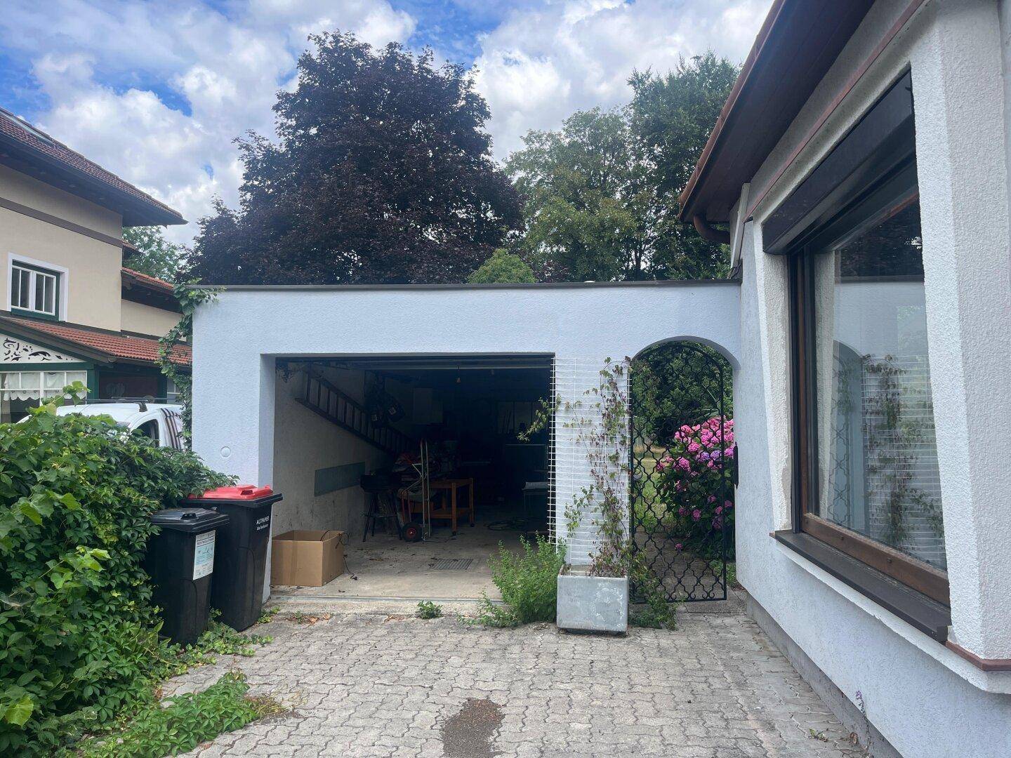 Offene Garage mit Einfahrt und einem kleinen Gartenbereich daneben.