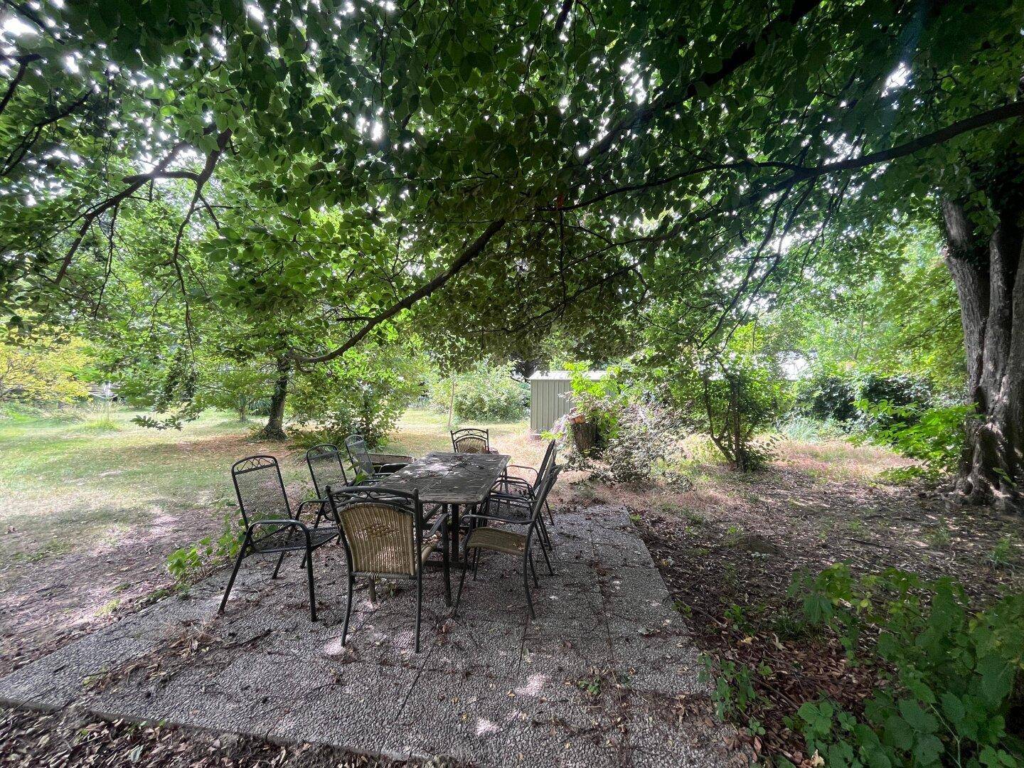 Gemütlicher Essbereich im Freien unter schattenspendenden Bäumen im Garten.