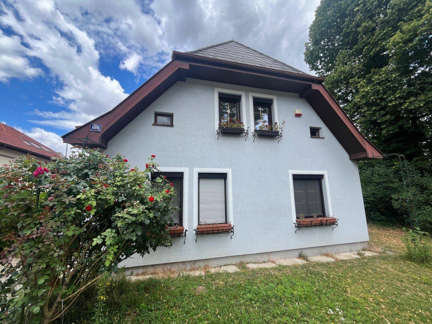 Seitenansicht des Hauses mit kleinen Fenstern und Blumenkästen unter blauem Himmel.