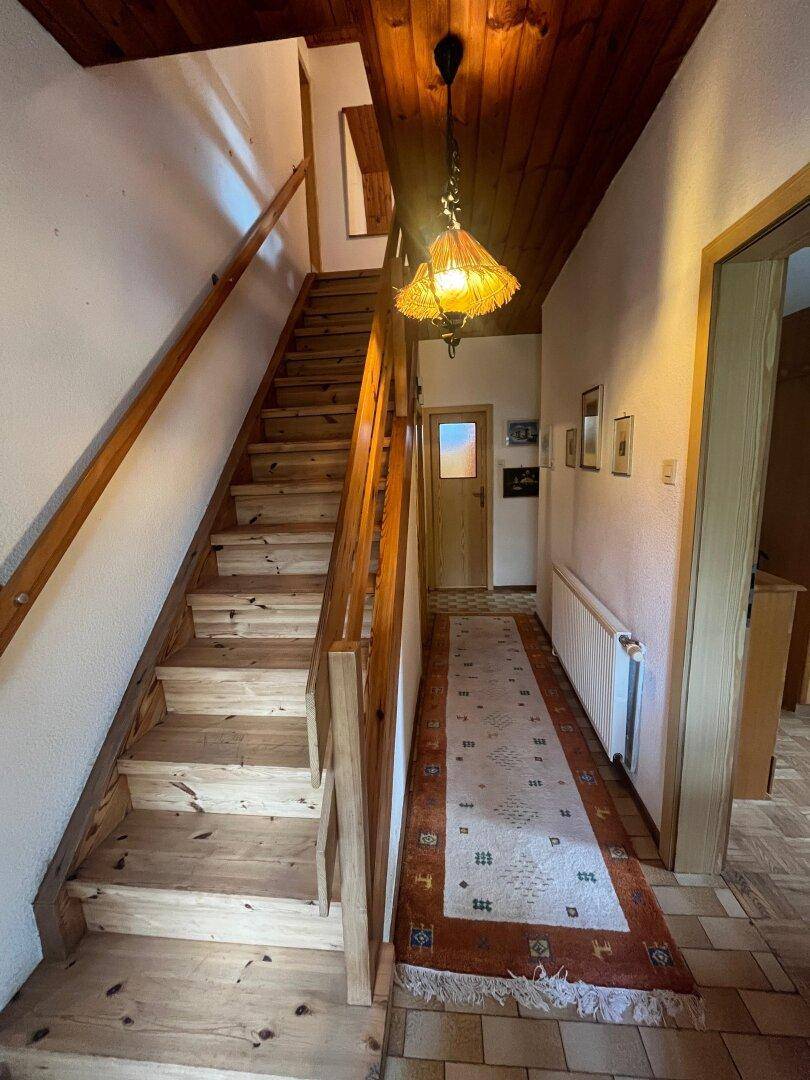 Heller Flur mit Holztreppe und Holzbalkendecke, die in die obere Etage führt.