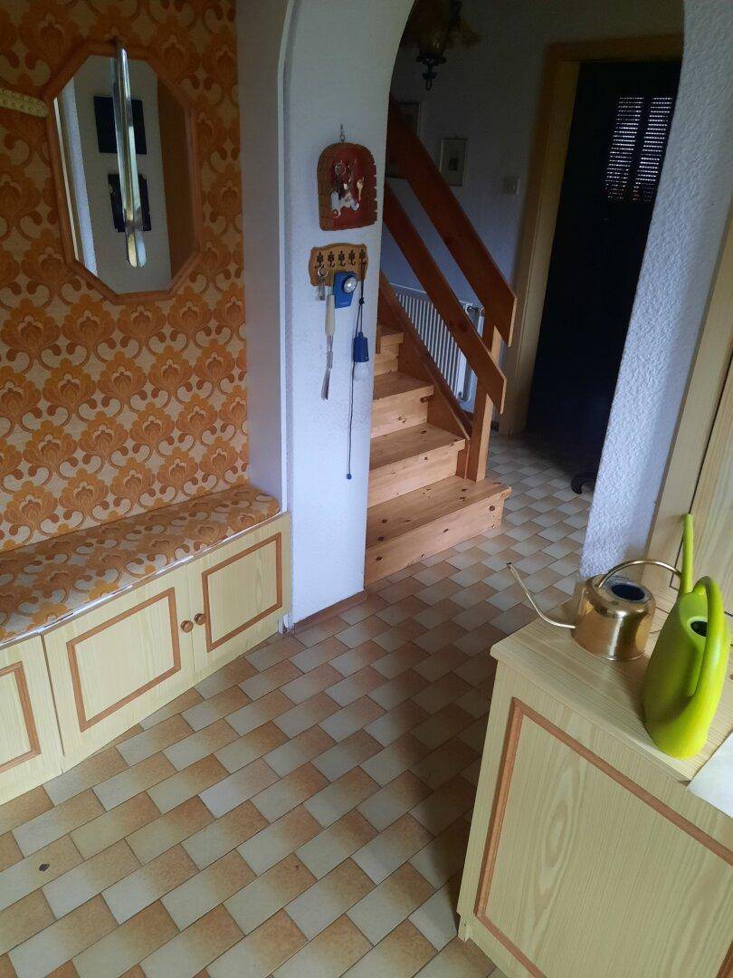Eingangsbereich mit gemusterten Fliesen, Holzbänken und Zugang zur Treppe.