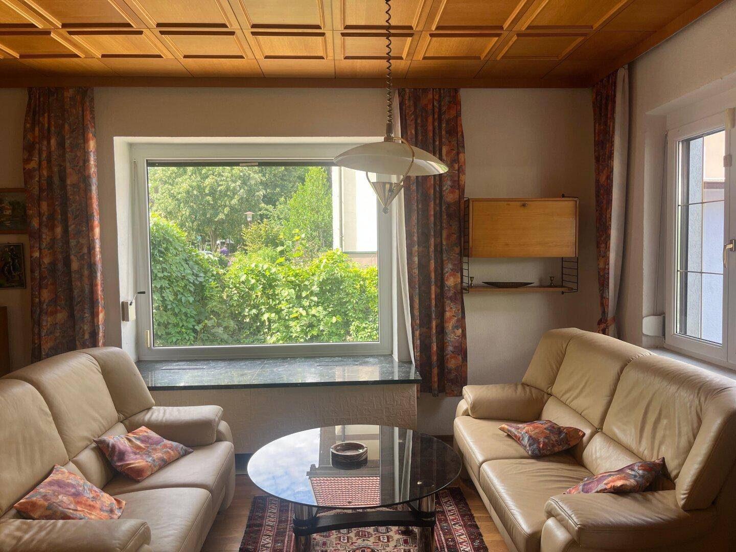 Helles Wohnzimmer mit beigen Ledersofas, Holzkassettendecke und Gartenblick.