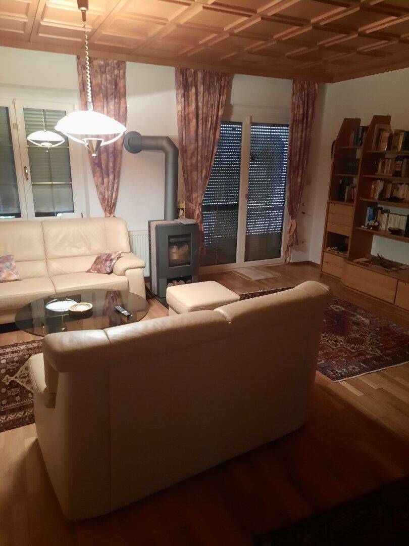 Wohnzimmer mit beigen Sofas, Holzofen und Zugang zur Terrasse durch große Fenster.