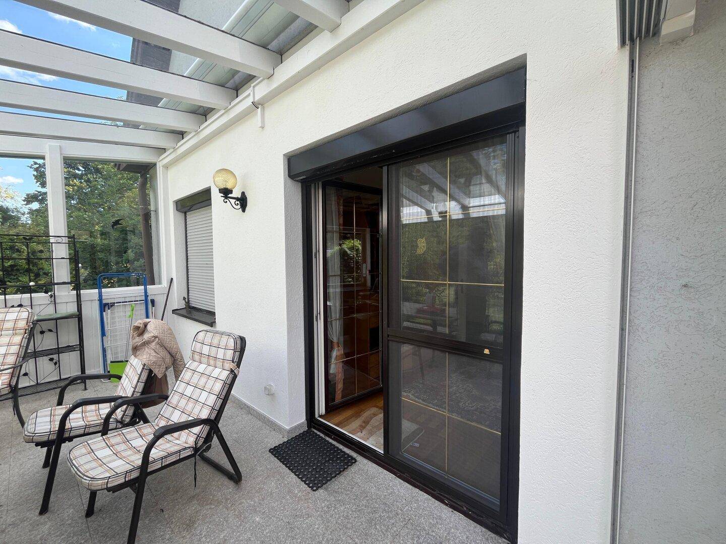 Überdachte Terrasse mit Gartenmöbeln und Zugang zum Innenbereich durch eine Schiebetür.