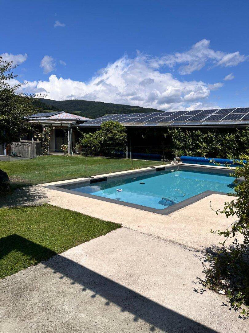 Außenbereich mit Swimmingpool, Rasenfläche und Photovoltaikanlage auf dem Dach des Gebäudes.