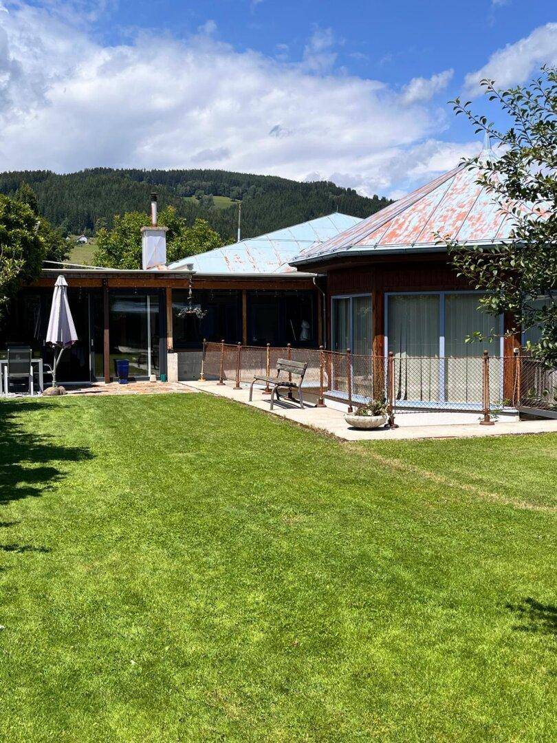 Weitläufiger Rasenbereich vor dem Haus mit Terrasse und Panoramablick auf die Berge.