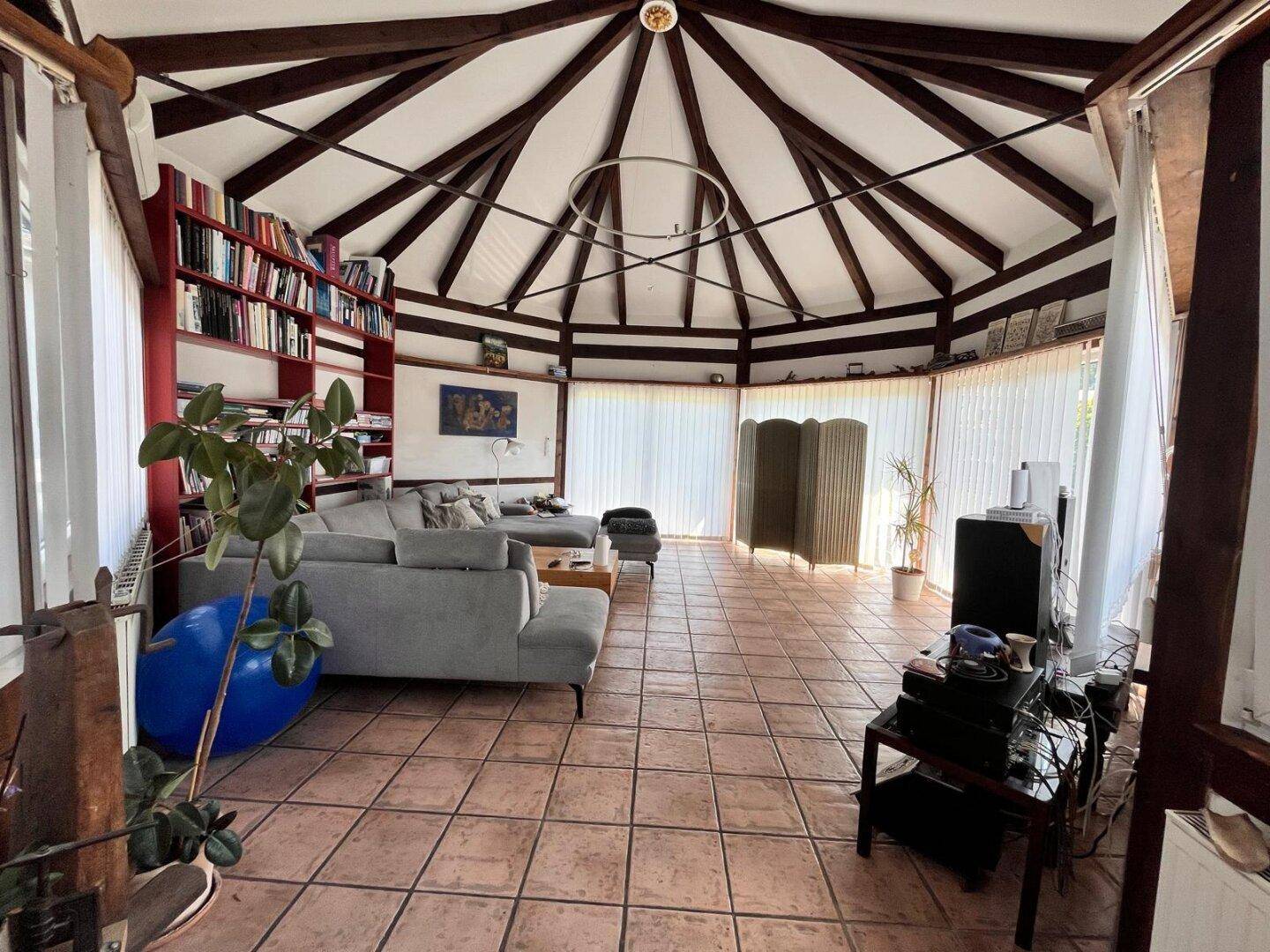 Weitläufiges Wohnzimmer mit gemütlicher Sitzecke, Bücherregal und einzigartiger Deckenkonstruktion.