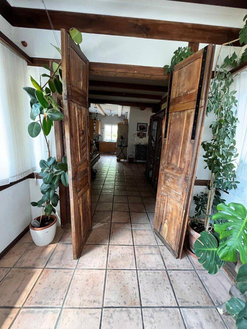 Heller Eingangsbereich mit Terrakottafliesen und Holzbalken, der zu einem weiteren Raum führt.