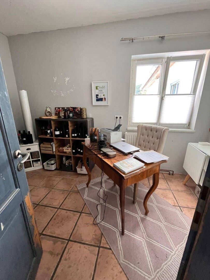 Helles Arbeitszimmer mit Terrakottafliesen, Holztisch und Fenster mit Blick nach draußen.