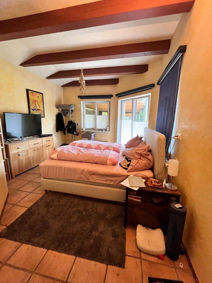 Gemütliches Schlafzimmer mit Terrakottafliesen, Holzbalken und Doppelbett, mit Zugang nach draußen.