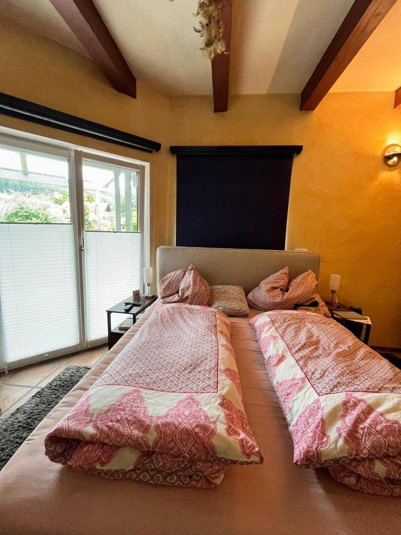 Helles Schlafzimmer mit Doppelbett, Terrakottafliesen und großen Fenstern, die viel Licht hereinlassen.