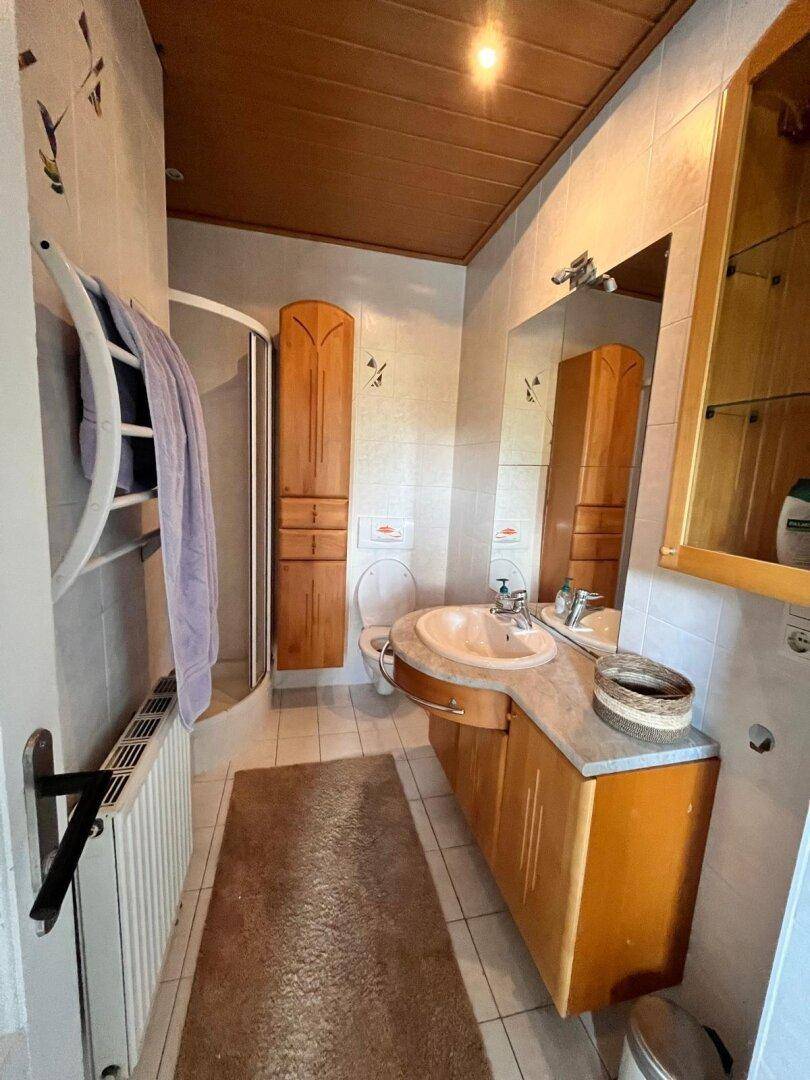 Badezimmer mit Waschtisch, Spiegel, Dusche und Holzschränken, in hellem Design.