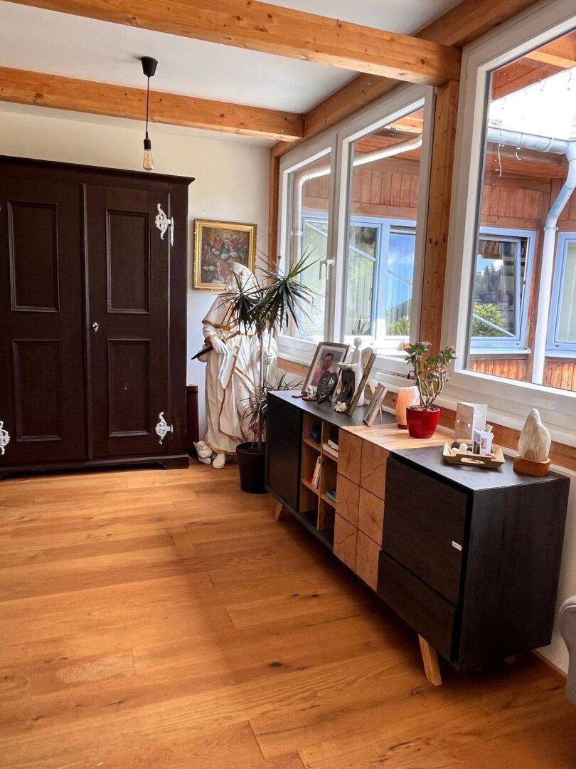 Heller Raum mit Holzboden, großen Fenstern und einem dunklen Schrank, der viel Tageslicht bietet.