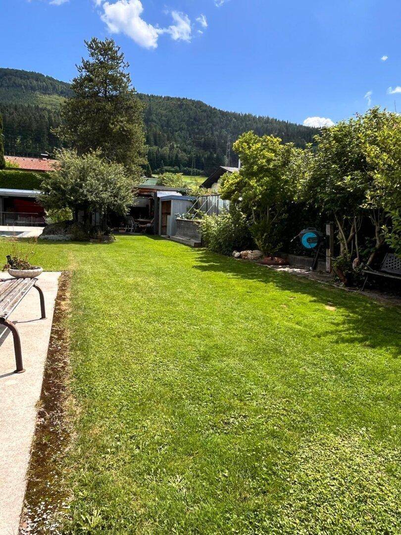 Weitläufiger Garten mit Rasenfläche, Bäumen und einem kleinen Geräteschuppen im Hintergrund.