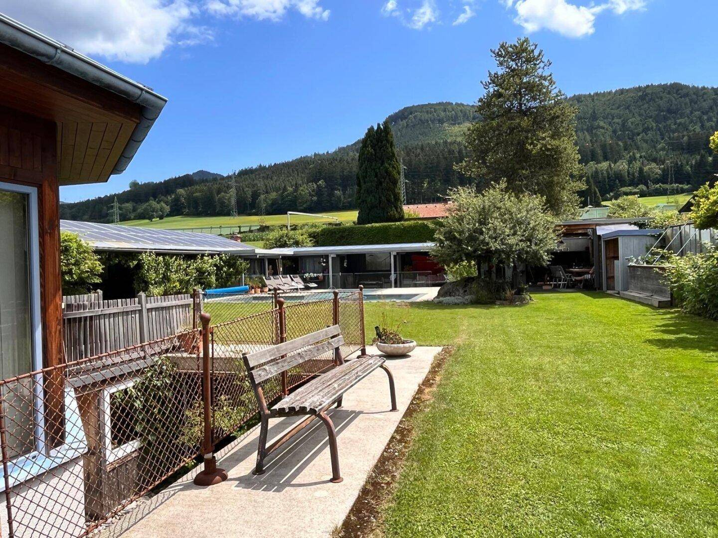 Grüner Gartenbereich mit einer Holzbank und Blick auf die umliegende Berglandschaft.