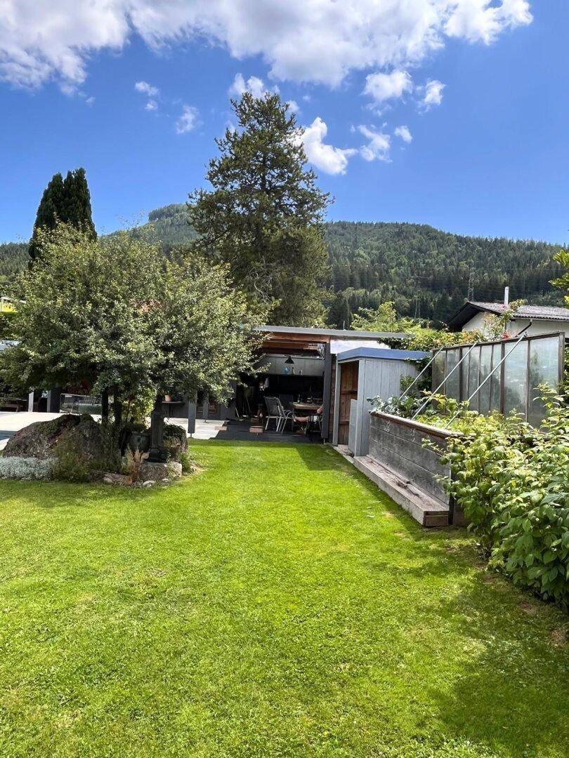 Gepflegter Garten mit Rasenfläche und Blick auf eine überdachte Terrasse und die umliegende Natur.