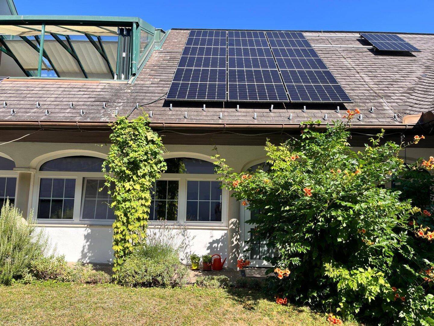 Hausfassade mit Photovoltaikanlage auf dem Dach und dekorativen Rundbogenfenstern.